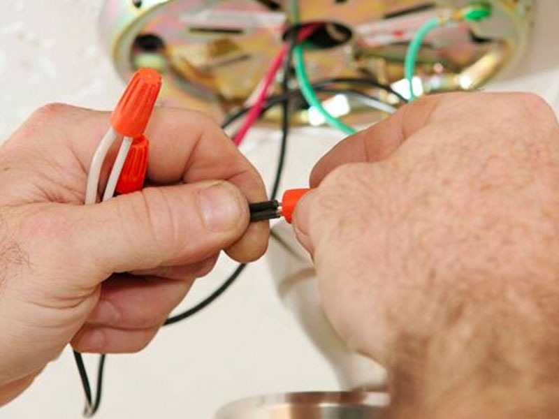 Electrician connecting wires from an exposed ceiling fan