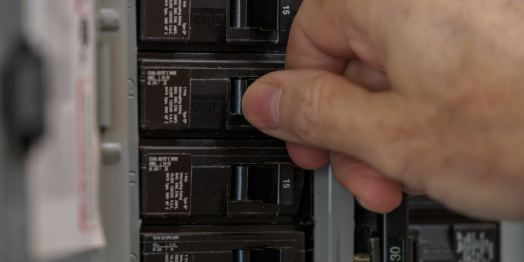 Closeup image of a hand resetting a circuit breaker in an electrical panel