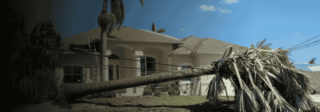 Is Your Home’s Electrical System Prepared for Hurricane Season? Residential home with roof damage from a hurricane and a fallen palm tree on power lines.