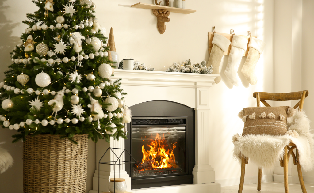 Cozy living room decorated for Christmas with a lit tree, white stockings hanging above a fireplace, and soft neutral furnishings.